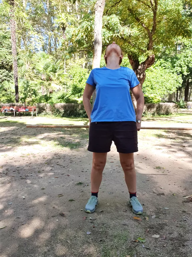 Mujer en ropa deportiva mirando hacia arriba en un parque, rodeada de árboles