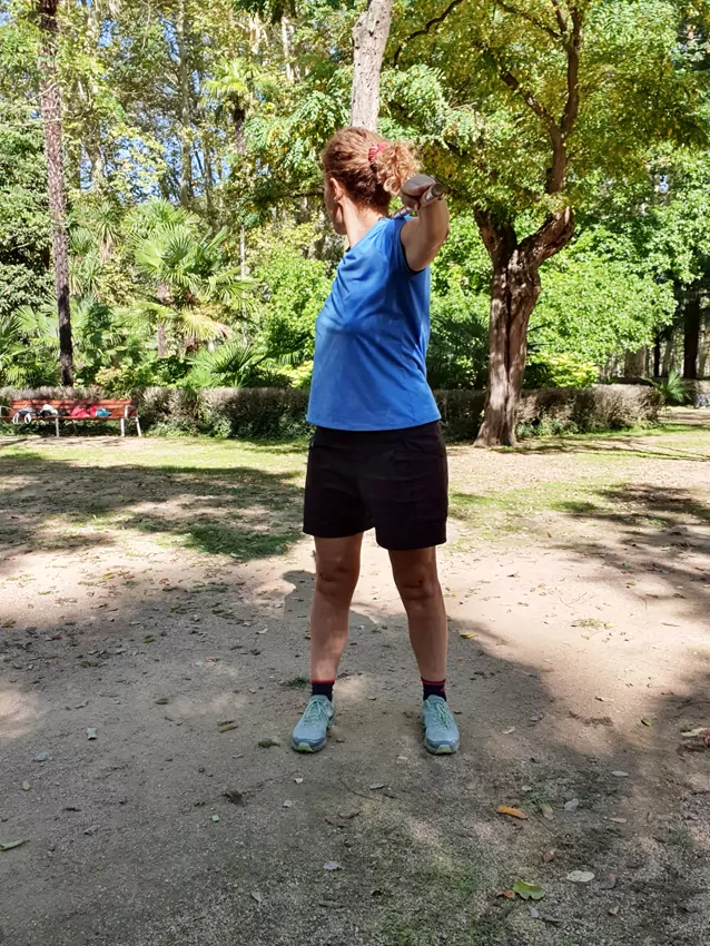 Mujer con ropa deportiva girando el torso con un bastón en un parque soleado