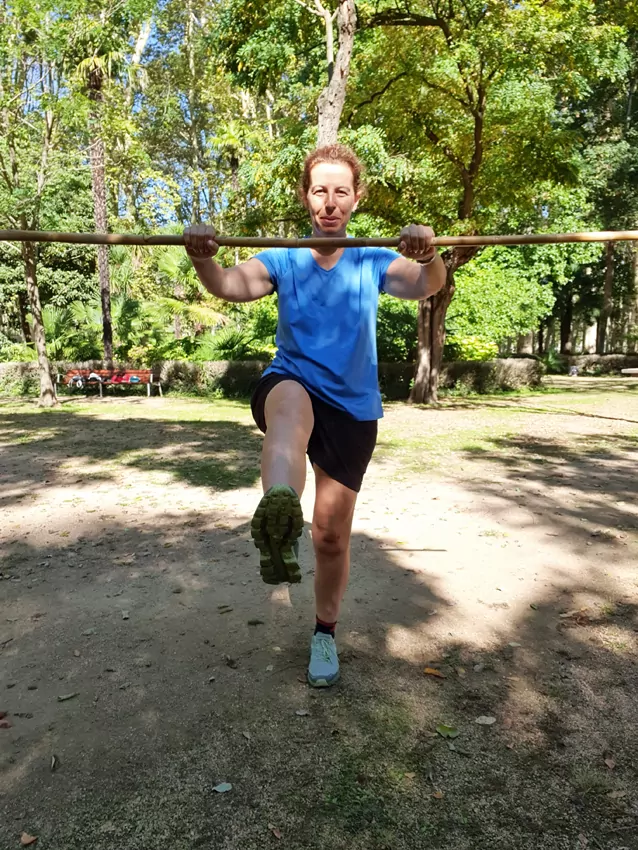 Mujer realizando ejercicio con un bastón en un parque, levantando una pierna